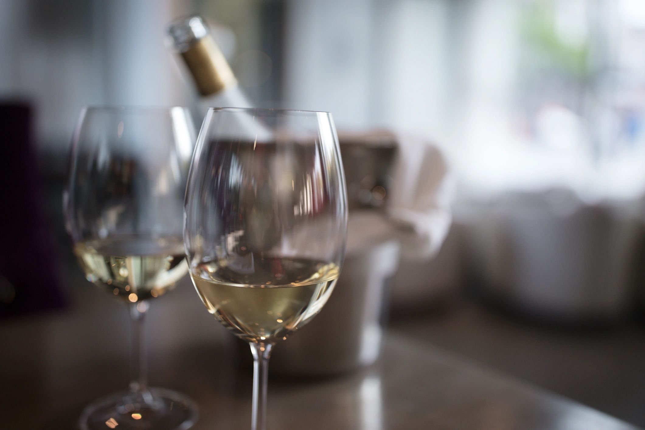 Two glasses of white wine on a table with an ice bucket in the background